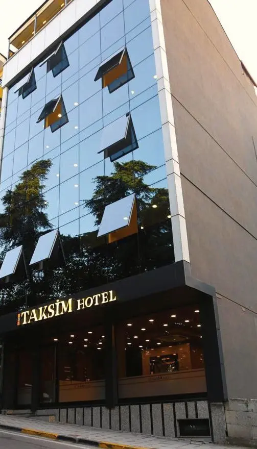 Otelin cam giydirme cephesi; camda ağaç yansımaları, girişte ışıklı tabela